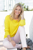 A blonde woman wearing a yellow jumper and white trousers