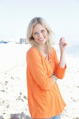 A blonde woman by the sea wearing an orange tunic