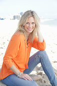 A blonde woman by the sea wearing an orange tunic and jeans