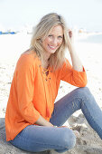 A blonde woman by the sea wearing an orange tunic and jeans