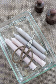 Pastel-coloured candles and scissors in glass dish