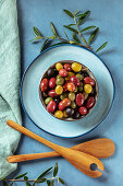 A variety of green, black and red olives, with leaves and wooden spoons