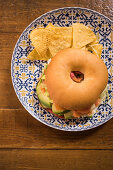 Tasty salmon bagel with tomato tartar and pickles placed on wooden table in kitchen