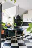 Table with black top and upholstered chairs in kitchen with chequered floor