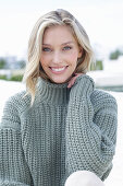 A young blonde woman on the beach wearing a grey knitted jumper