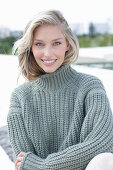 A young blonde woman on the beach wearing a grey knitted jumper