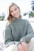 A young blonde woman on the beach wearing a grey knitted jumper