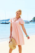 A blonde woman by the sea wearing a pink summer dress