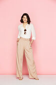 A brunette woman wearing wearing a white blouse and pink Marlene trousers