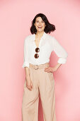 A brunette woman wearing wearing a white blouse and pink Marlene trousers