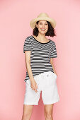A brunette woman wearing a straw hat, a striped t-shirt and white shorts