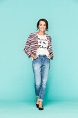 A dark-haired woman wearing a t-shirt, a striped jacket and jeans