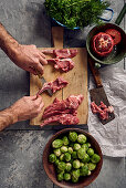 Lamb chops being deboned with a knife next to Brussels sprouts and herbs