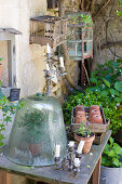 Glass bell over a plant on an old table in a garden with an assortment of objects