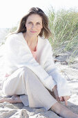 Langhaarige Frau in hellem Pullover und Hose im Sand am Strand