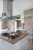 Extractor hood above hob on island counter in kitchen with brick wall