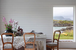 Dining table and rustic chairs in room with white-painted wood panelling