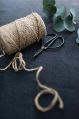 Twine, scissors and eucalyptus branch on a dark surface