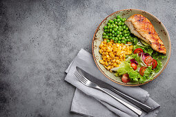 Baked chicken breast with fresh salad, green peas and corn