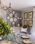 Gedeckter runder Tisch unter französischem Kronleuchter, Teller und botanische Drucke an den Wänden