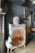 Vase of twigs in open-topped cabinet and vintage accessories against grey wall