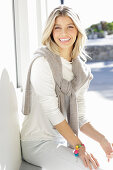 A young blonde woman wearing a white top with a jumper over her shoulders