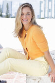 A young blonde woman wearing an orange cardigan and a pair of light trousers