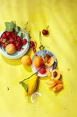 Zitronen, Aprikosen und frische Beeren auf gelbem Untergrund