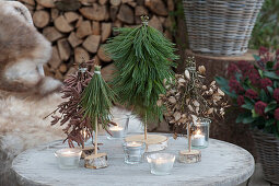 Small crafted pine trees for Christmas table decorations: bound trees made of pine, maple, and hazel branches and lanterns on a round garden table