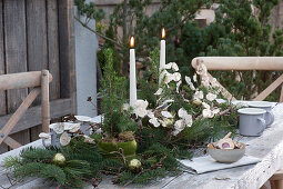Weihnachts-Tischdeko auf der Terrasse: Kerzen, Zuckerhutfichten in Filztopf, Tannenzweige, Silbertaler und Christbaumkugeln