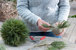 Christmas tree ornaments in forest motif: Woman puts pine twigs into a ball
