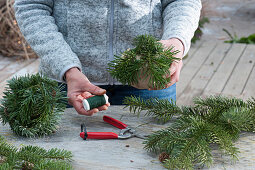 Christmas tree ornaments in forest motif: Woman wraps paper ball with pine twigs