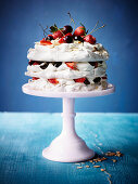 Amaretto-Baisertorte mit Erdbeeren und Kirschen vor blauem Hintergrund