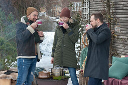 Friends standing comfortably around the barbecue drinking hot mulled cider, pots of cider on the barbecue