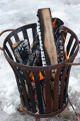 Fire basket with burning logs in the snow