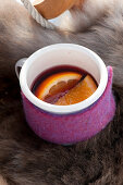 Cup with hot mulled wine wrapped with felt resting on fur
