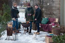 Friends standing comfortably around firepit and toasting stick bread, dog Zula