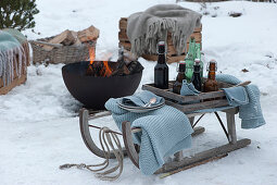 Wooden crate with beer bottles and water bottles on a wooden sled, firepit in the background