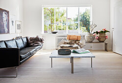 Black leather sofa, coffee table with marble top and designer chair in a light living room