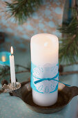 Weißer Kerze mit blauem Seidenpapier und Tortenspitze dekoriert