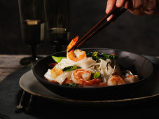 Man’s Hand With Chopsticks Holding Shrimp in Bowl of Noodles