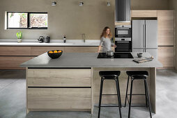 Bar stools at island counter with hob; woman in background