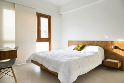 Double bed with wooden headboard and concrete floor in bedroom