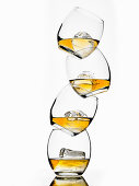 Vier Gläser Whiskey mit Eiswürfeln, gestapelt vor weißem Hintergrund