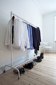 Shoes lined up below shirts hung on clothes rail