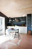 Breakfast table with various chairs in white fitted kitchen with black wall