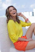 A dark-blonde woman wearing a yellow blouse and orange shorts