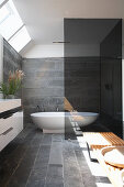 Free-standing bathtub in bathroom with slate tiles and skylight