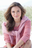 A young, long-haired woman wearing a pink blouse with a jumper over her shoulders