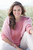 A young, long-haired woman wearing a pink blouse with a jumper over her shoulders